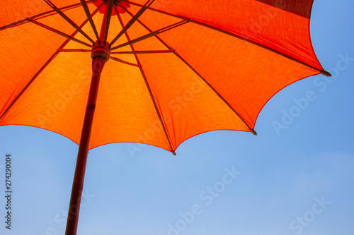 Orange color beach umbrella made of wooden for protected sunlight with a bright blue sky background. © Pina