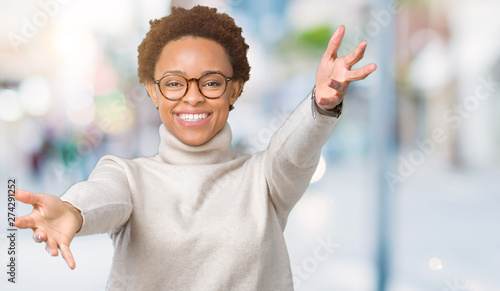 Young beautiful african american woman wearing glasses over isolated background looking at the camera smiling with open arms for hug. Cheerful expression embracing happiness. © Krakenimages.com