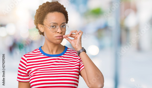 Beautiful young african american woman wearing glasses over isolated background mouth and lips shut as zip with fingers. Secret and silent  taboo talking