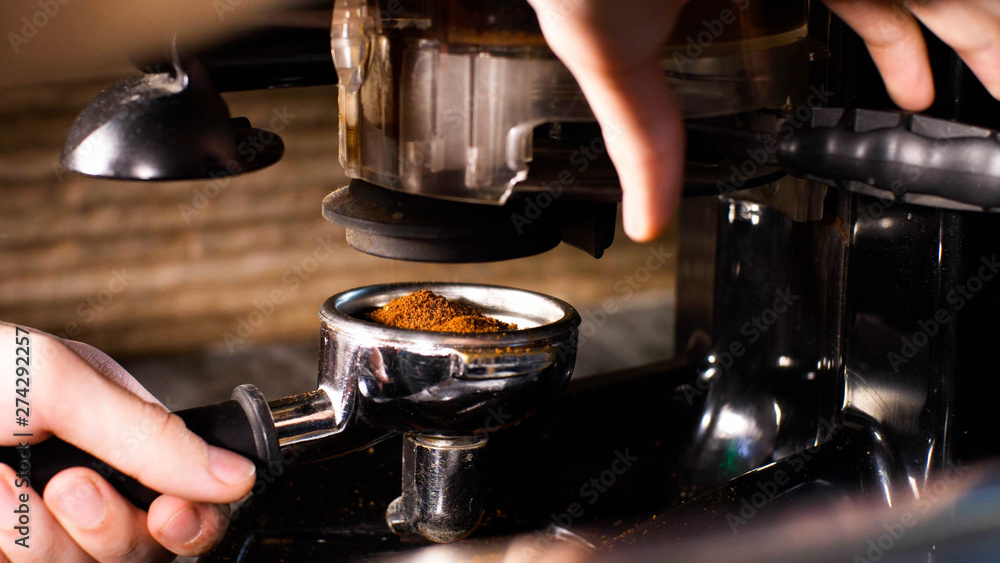 Barista man is grinding coffee using hand coffee grinder pushing handle, coffee pours into the holder, closeup hands.
