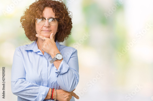 Beautiful middle ager senior businees woman wearing glasses over isolated background looking confident at the camera with smile with crossed arms and hand raised on chin. Thinking positive.