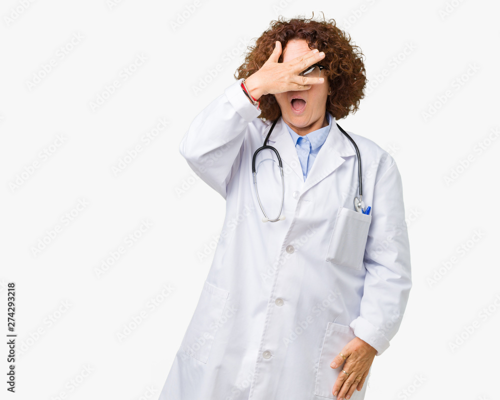Middle ager senior doctor woman over isolated background peeking in shock covering face and eyes with hand, looking through fingers with embarrassed expression. Middle ager senior doctor woman over isolated background peeking in shock covering face and eyes with hand, looking through fingers with embarrassed expression.