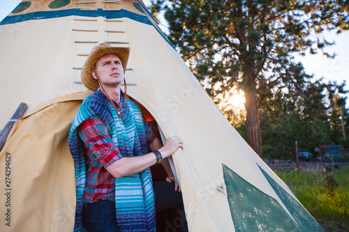 A man in a pancho and cowboy hat exits a tepee in northeast Oregon at sunset. photo