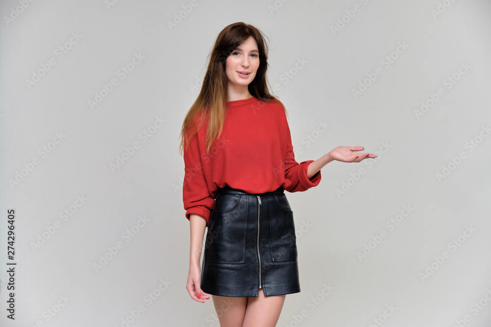Photo portrait of a beautiful pretty brunette girl in a red sweater on a gray background. A woman is satisfied with her life, she stands in front of the camera, smiling and talking. Made in a studio.