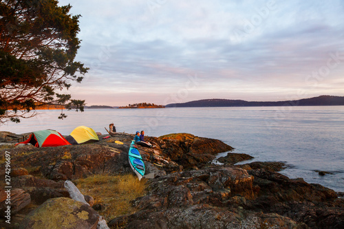 Two women enjoy a colorful sunset at a picturesque peninsula campsite in the south cove of Jones Island during a 3-day sea kayaking trip in the San Juan Isands of northwest Washington State. The island is a 188 acre State Park that is only accessible by boat and has 24 campsites. photo