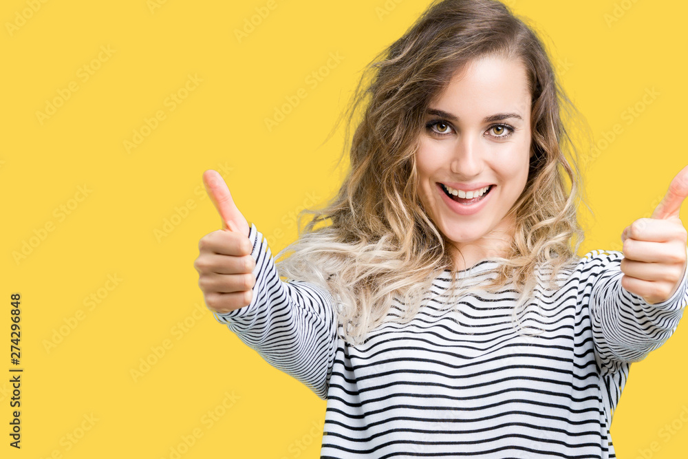 Beautiful young blonde woman wearing stripes sweater over isolated background approving doing positive gesture with hand, thumbs up smiling and happy for success. Looking at the camera Beautiful young blonde woman wearing stripes sweater over isolated background approving doing positive gesture with hand, thumbs up smiling and happy for success. Looking at the camera