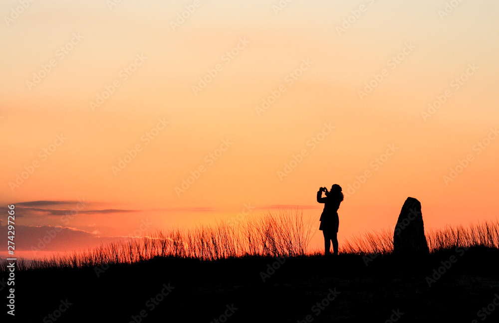 Silhouette of woman taking picture over sunset sky background