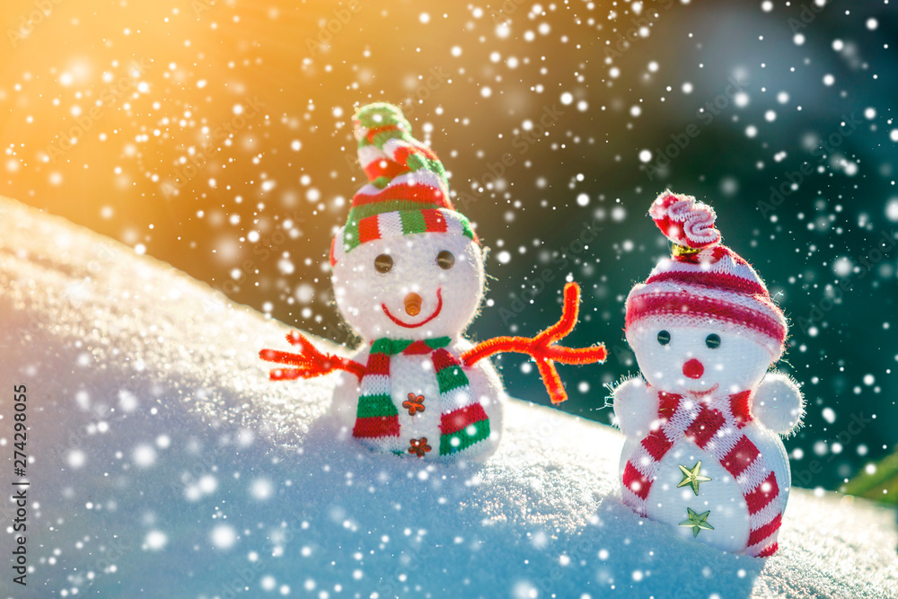 Two small funny toys baby snowman in knitted hats and scarves in deep snow outdoors on bright blue and white copy space background. Happy New Year and Merry Christmas greeting card. Two small funny toys baby snowman in knitted hats and scarves in deep snow outdoors on bright blue and white copy space background. Happy New Year and Merry Christmas greeting card.
