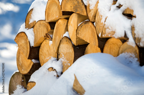 Neatly piled stack of chopped dry trunks wood covered with snow outdoors on bright cold winter sunny day, abstract background, Fire wood logs prepared for winter, ready for burning.