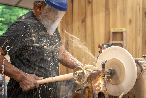 An African American older man creates works of art through bowl turning on a lathe. This shows him working and standing by the machine. photo