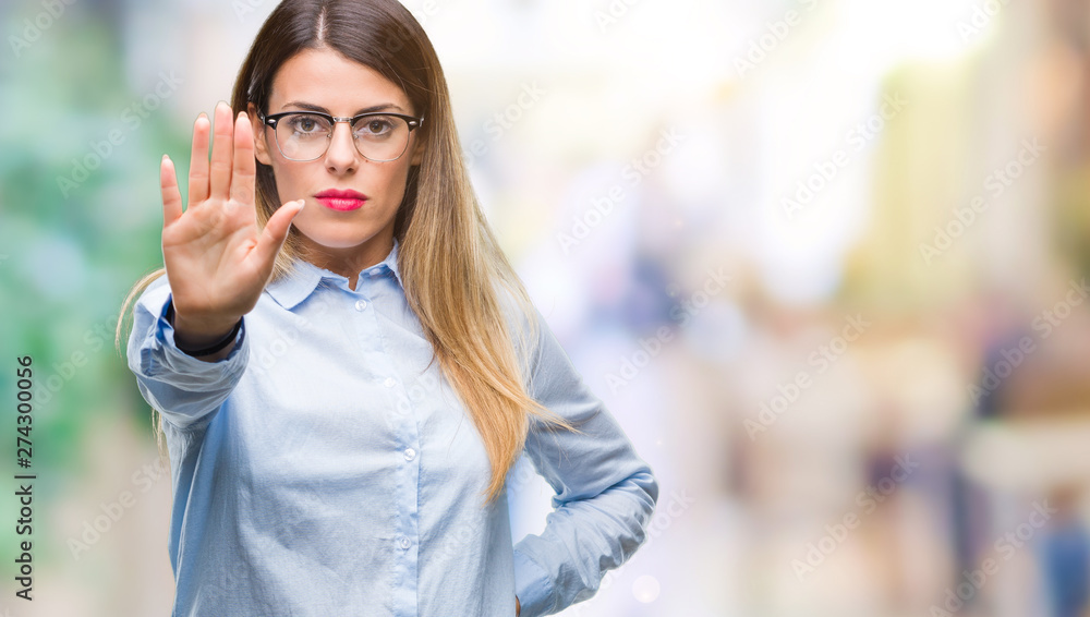 Young beautiful business woman wearing glasses over isolated background doing stop sing with palm of the hand. Warning expression with negative and serious gesture on the face.