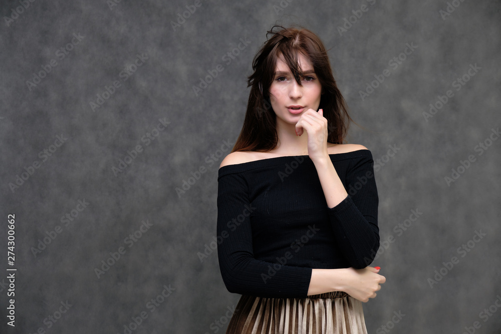 Photo portrait of a beautiful pretty brunette girl in a black sweater on a gray background. A woman is satisfied with her life, she stands in front of the camera, smiling and talking. Made in studio. Photo portrait of a beautiful pretty brunette girl in a black sweater on a gray background. A woman is satisfied with her life, she stands in front of the camera, smiling and talking. Made in studio.