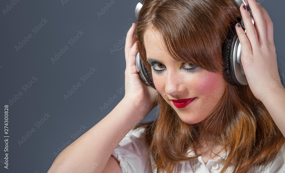 Entertainment redhead girl with helmet on her head listening to music on a flat gray background Entertainment redhead girl with helmet on her head listening to music on a flat gray background