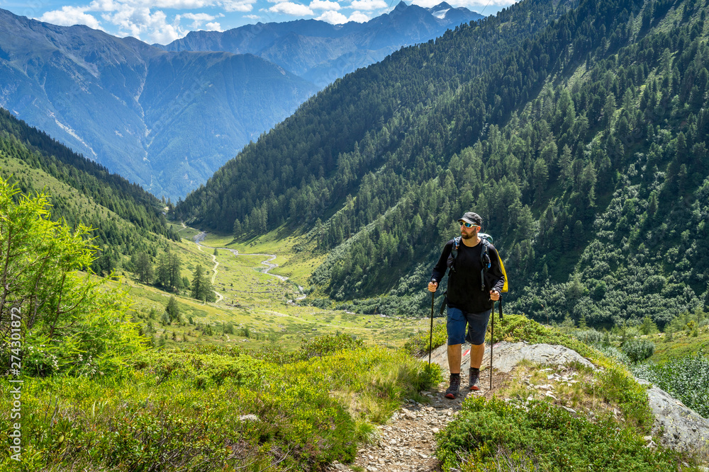 Man hiking up a trail with mountains in the background Man hiking up a trail with mountains in the background