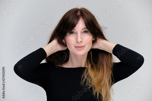 Beauty portrait of a beautiful pretty brunette girl in a black sweater on a light gray background. A woman is happy with life, she is standing in front of the camera, smiling. Made in a studio.