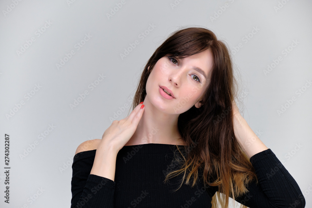 Beauty portrait of a beautiful pretty brunette girl in a black sweater on a light gray background. A woman is happy with life, she is standing in front of the camera, smiling. Made in a studio. Beauty portrait of a beautiful pretty brunette girl in a black sweater on a light gray background. A woman is happy with life, she is standing in front of the camera, smiling. Made in a studio.
