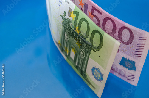 500 and 100 euro banknotes on a blue background reflecting