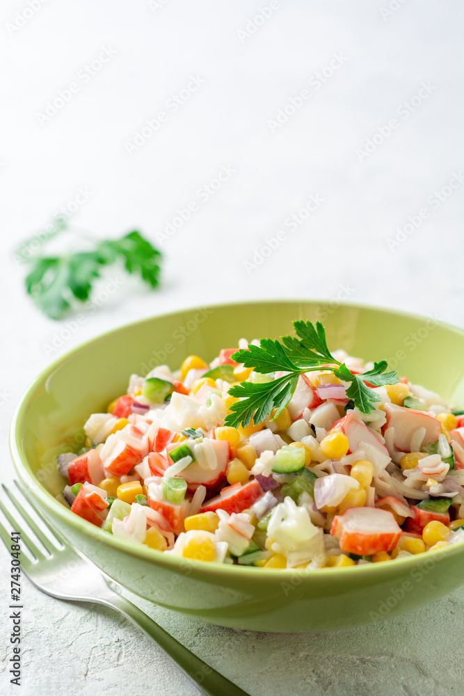 Salad with crab sticks, sweet corn, cucumbers, boiled eggs, onion and rice in bowl on concrete background. Russian cuisine. Selective focus. Salad with crab sticks, sweet corn, cucumbers, boiled eggs, onion and rice in bowl on concrete background. Russian cuisine. Selective focus.