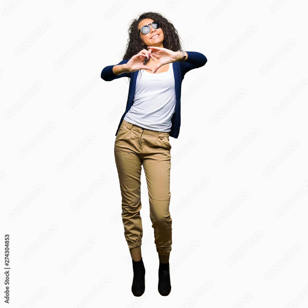 Young beautiful girl with curly hair wearing fashion sunglasses smiling in love showing heart symbol and shape with hands. Romantic concept. Young beautiful girl with curly hair wearing fashion sunglasses smiling in love showing heart symbol and shape with hands. Romantic concept.