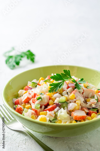 Salad with crab sticks, sweet corn, cucumbers, boiled eggs, onion and rice in bowl on concrete background. Russian cuisine. Selective focus.