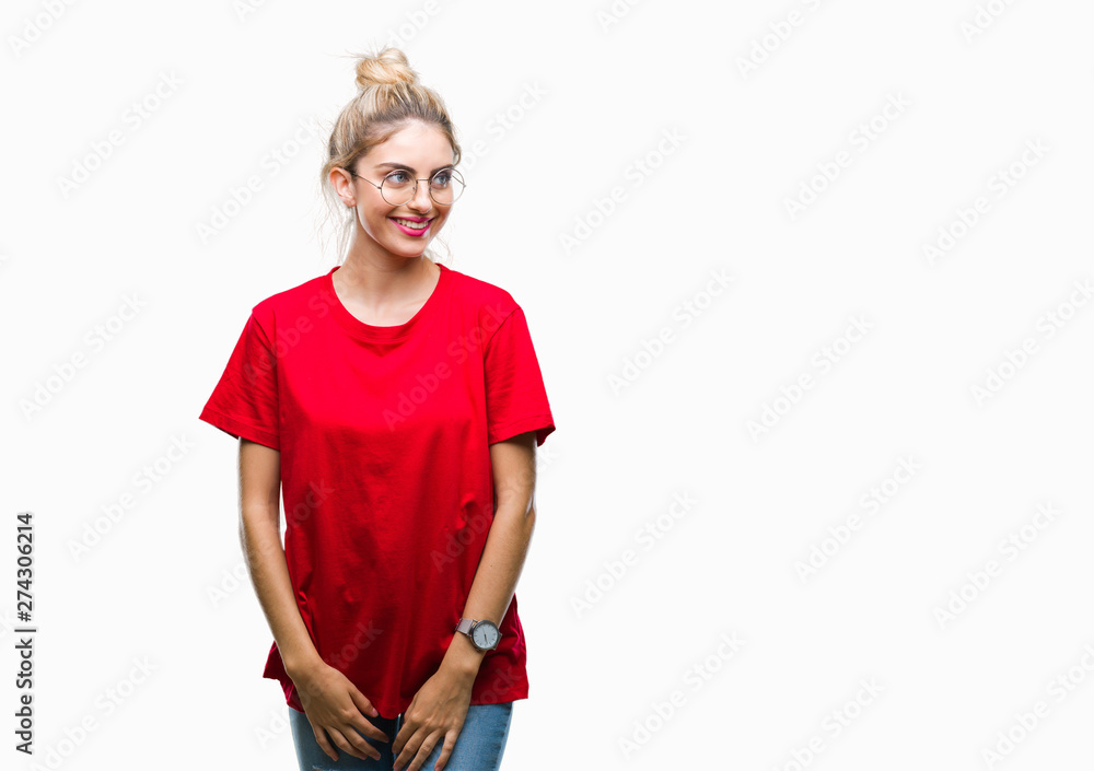 Fototapeta premium Young beautiful blonde woman wearing red t-shirt and glasses over isolated background looking away to side with smile on face, natural expression. Laughing confident.