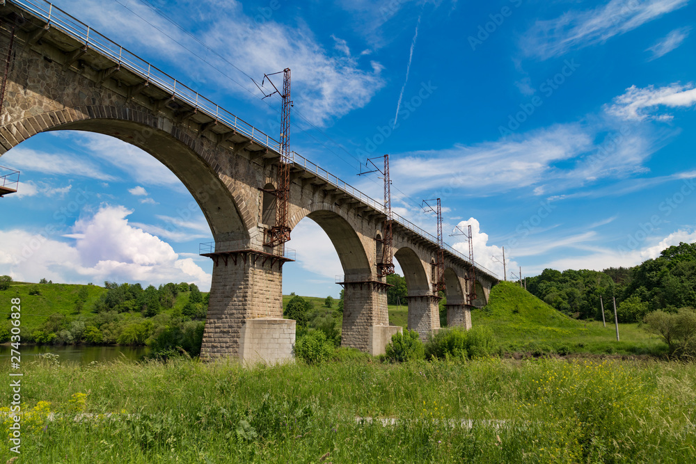 Fototapeta premium Beautiful old arched stone railway bridge against the backdrop of a scenic landscape