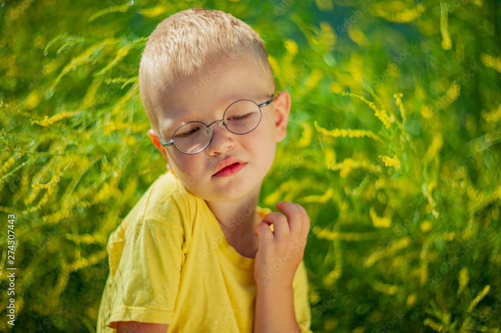 Portrait of charming boy in yellow T-shirt and glasses against background of green flowering bush. child examines flowers through magnifying glass. Spring floral background. soft lens Portrait of charming boy in yellow T-shirt and glasses against background of green flowering bush. child examines flowers through magnifying glass. Spring floral background. soft lens