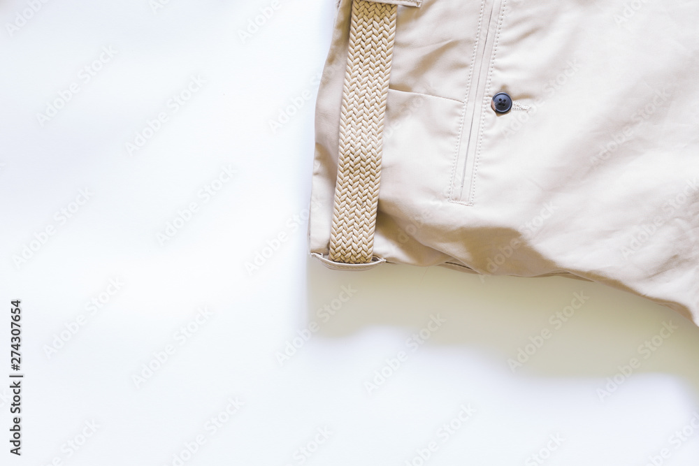 Close-up shot of pants made from a soft beige material with brown button and knitted belt on white background – Stylish shorts from khaki fabric with copy space