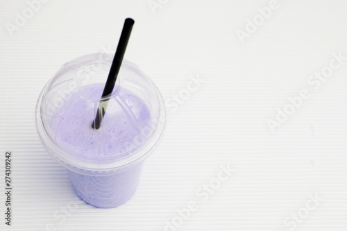 Milk and blueberries cocktail with a straw in a plastic glass on a light background with space for text.