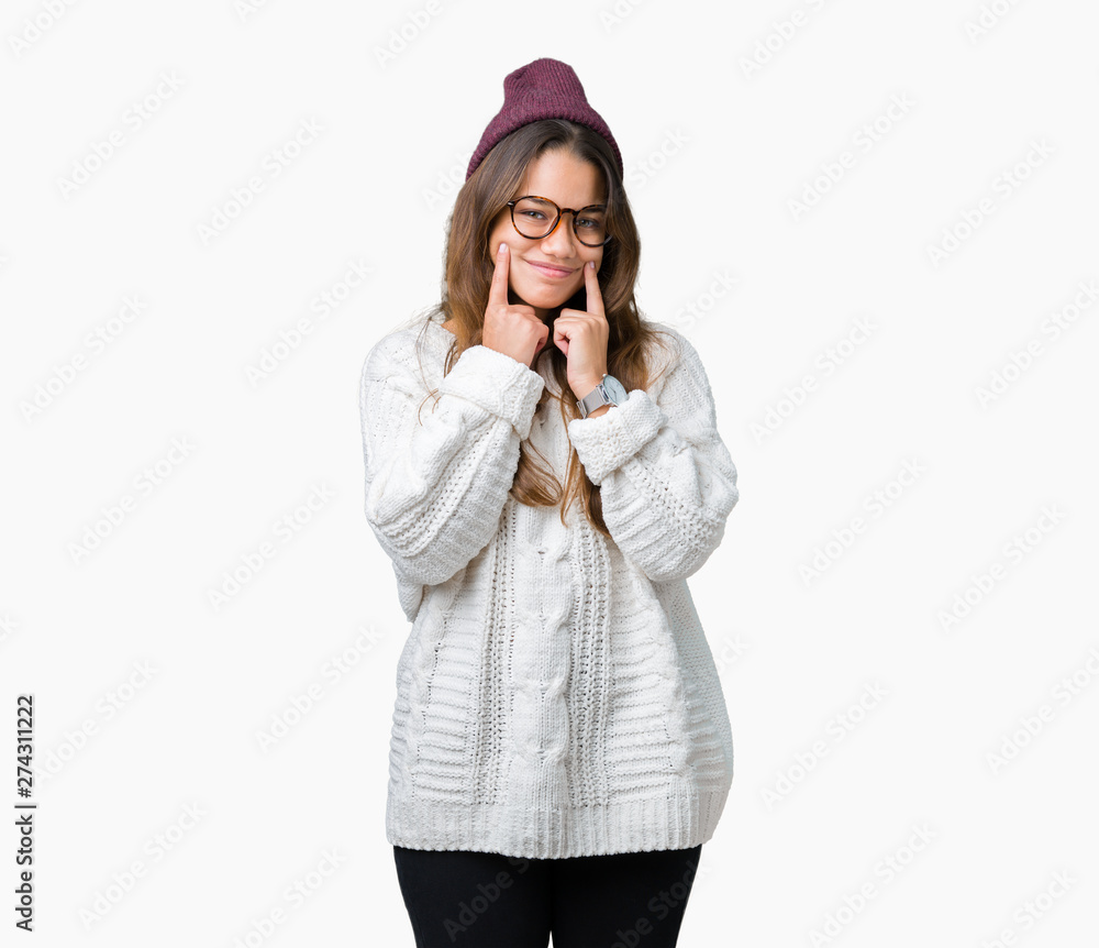 Fototapeta premium Young beautiful brunette hipster woman wearing glasses and winter hat over isolated background Smiling with open mouth, fingers pointing and forcing cheerful smile