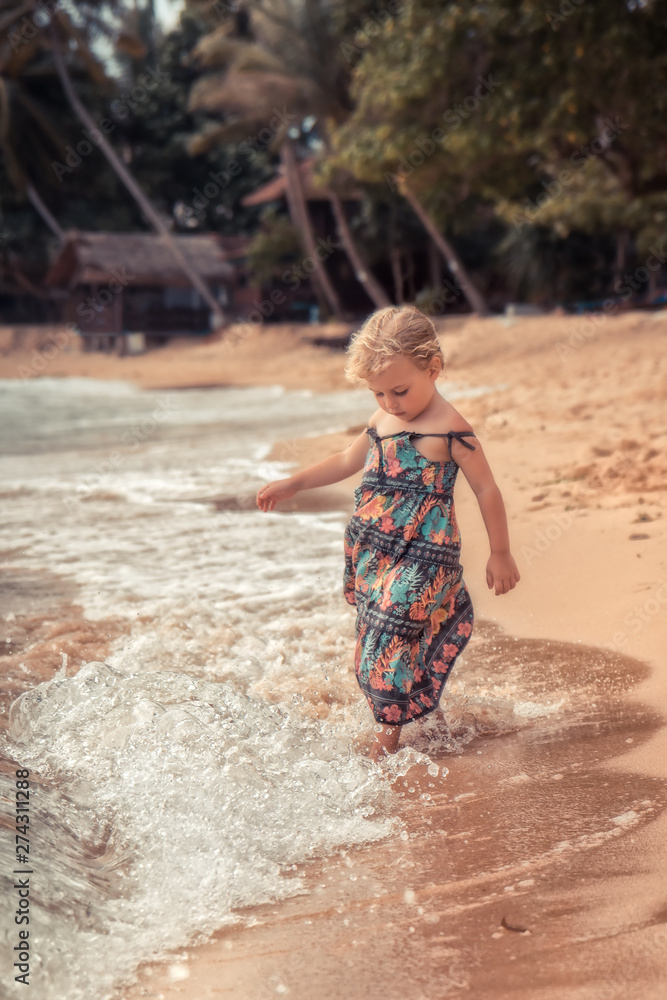 Beautiful child girl playing with waves on beach tropical island during summer holidays concept carefree childhood travel lifestyle Beautiful child girl playing with waves on beach tropical island during summer holidays concept carefree childhood travel lifestyle
