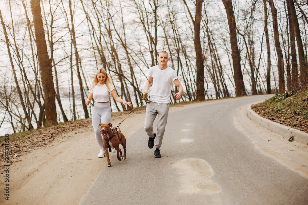 Beautiful couple in a park. Sportsman in a sportswear. Couple with a dog Beautiful couple in a park. Sportsman in a sportswear. Couple with a dog