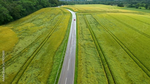 Red car driving at asphalt road with green fields at both sides. Seen from above, drone view photo
