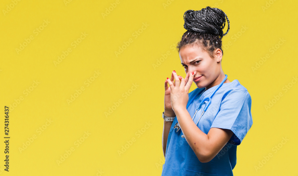 Young braided hair african american girl professional surgeon over isolated background smelling something stinky and disgusting, intolerable smell, holding breath with fingers on nose