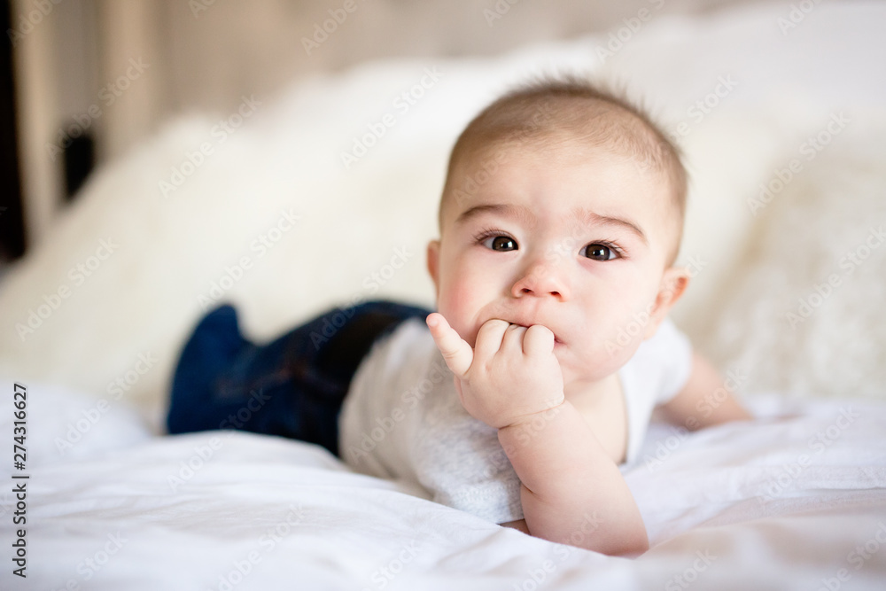 Cute brown eyed baby boy laying on bed with fingers in mouth Cute brown eyed baby boy laying on bed with fingers in mouth