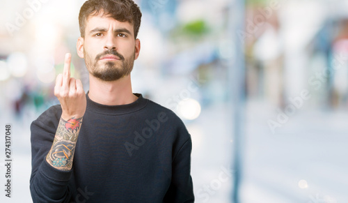 Young handsome man over isolated background Showing middle finger, impolite and rude fuck off expression