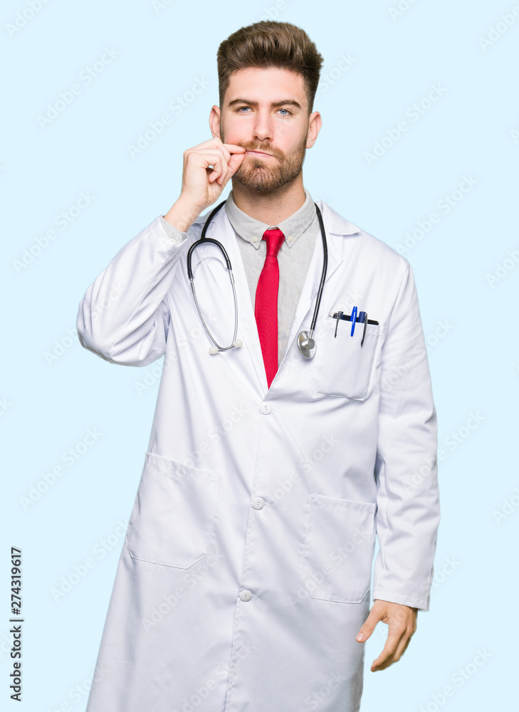 Young handsome doctor man wearing medical coat mouth and lips shut as zip with fingers. Secret and silent, taboo talking Young handsome doctor man wearing medical coat mouth and lips shut as zip with fingers. Secret and silent, taboo talking