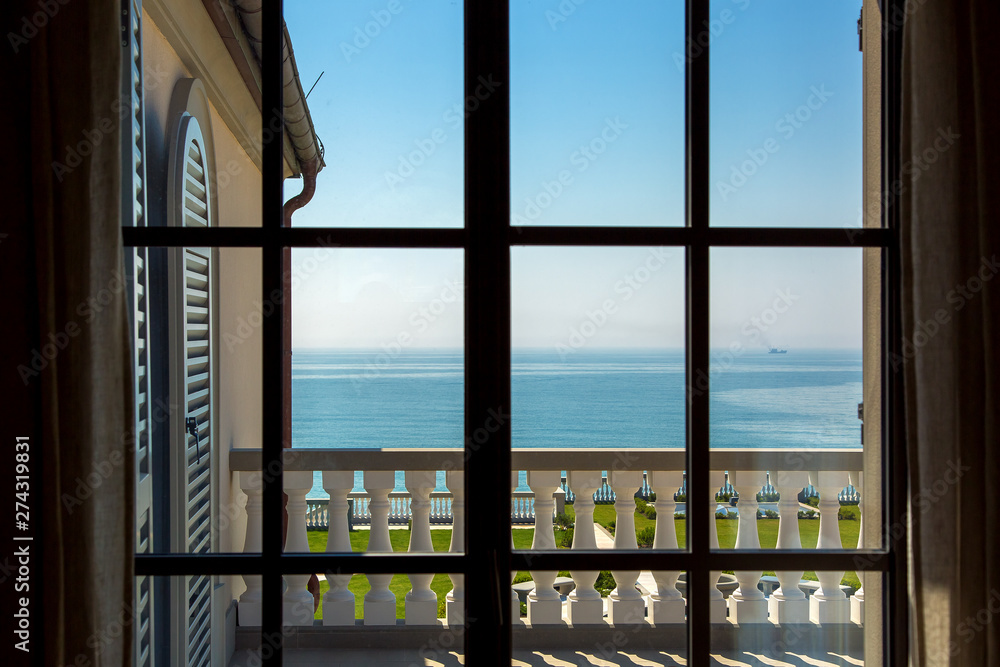Fototapeta premium view from the window inside the room on the balcony with balustrades and wooden shutters in the background blue sky with the sea summer sunny morning nobody.