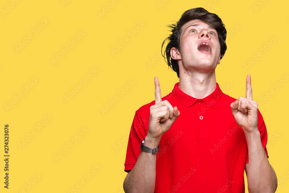 Young handsome man wearing red t-shirt over isolated background amazed and surprised looking up and pointing with fingers and raised arms. Young handsome man wearing red t-shirt over isolated background amazed and surprised looking up and pointing with fingers and raised arms.