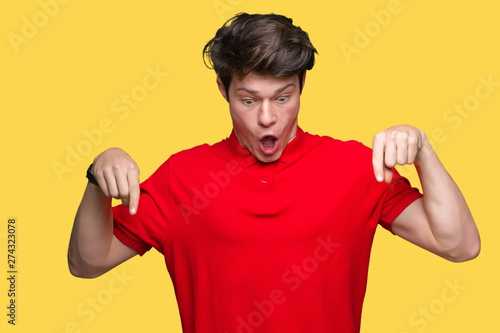 Young handsome man wearing red t-shirt over isolated background Pointing down with fingers showing advertisement, surprised face and open mouth © Krakenimages.com