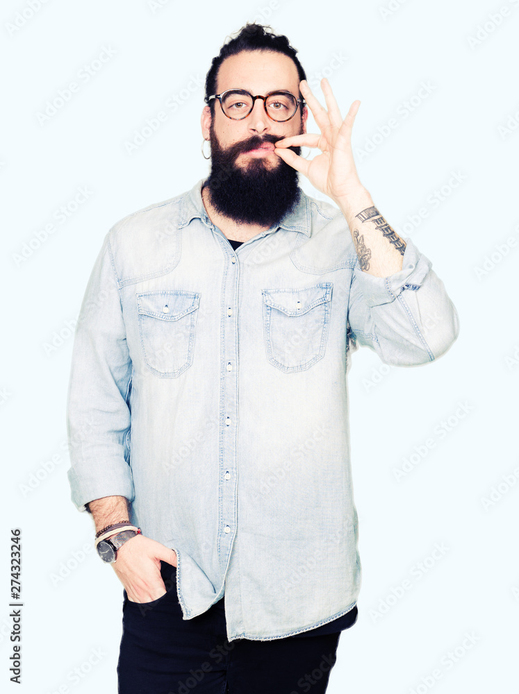 Young hipster man with long hair and beard wearing glasses mouth and lips shut as zip with fingers. Secret and silent, taboo talking Young hipster man with long hair and beard wearing glasses mouth and lips shut as zip with fingers. Secret and silent, taboo talking