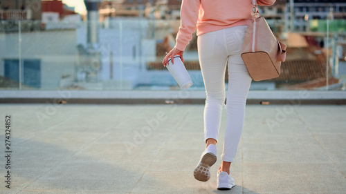 Close-up of young woman walking with a white thermo mug in hands.
