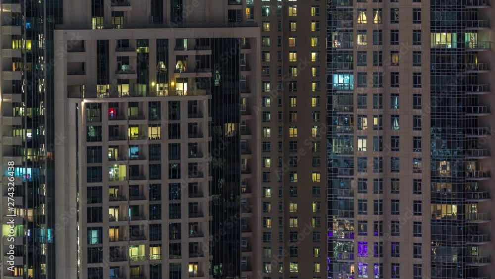 Windows of the multi-storey building with lighting inside and moving people in apartments timelapse. Aerial view of modern residential skyscrapers in Dubai downtown. Pan up Windows of the multi-storey building with lighting inside and moving people in apartments timelapse. Aerial view of modern residential skyscrapers in Dubai downtown. Pan up