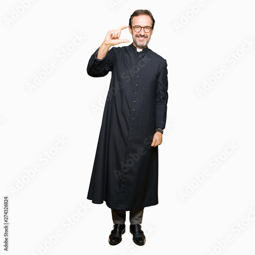 Middle age priest man wearing catholic robe smiling and confident gesturing with hand doing size sign with fingers while looking and the camera. Measure concept.