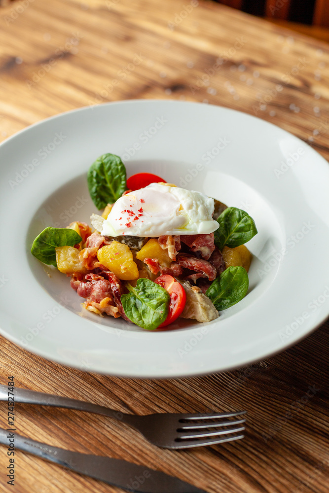 Rustic salad with, tomatoes, chorizo sausage, poached egg, spinach, potato and pickled cucumber for nutritious dinner, served on wooden table Rustic salad with, tomatoes, chorizo sausage, poached egg, spinach, potato and pickled cucumber for nutritious dinner, served on wooden table