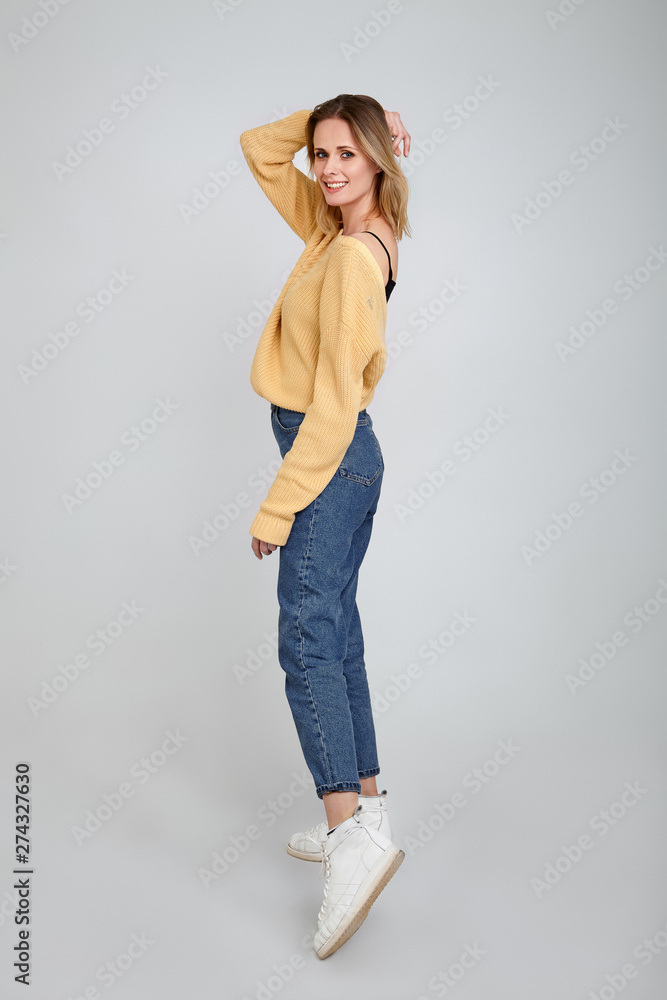 Slim and beautiful. Full length studio shot of attractive young woman in casual wear smiling and holding hair by her hand while standing against grey background Slim and beautiful. Full length studio shot of attractive young woman in casual wear smiling and holding hair by her hand while standing against grey background