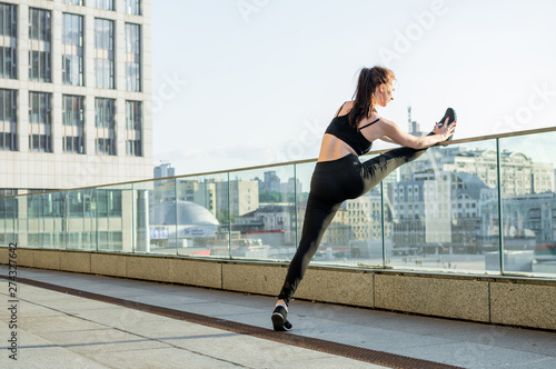 athletic girl engaged in athletics on the background of the city  she trains in the morning on the street  a woman does stretching and gymnastic tricks