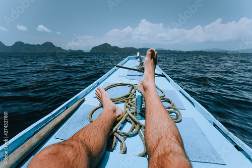Legs of man on banca boat approaching tropical island. travel, summer exotic vacation holidays concept