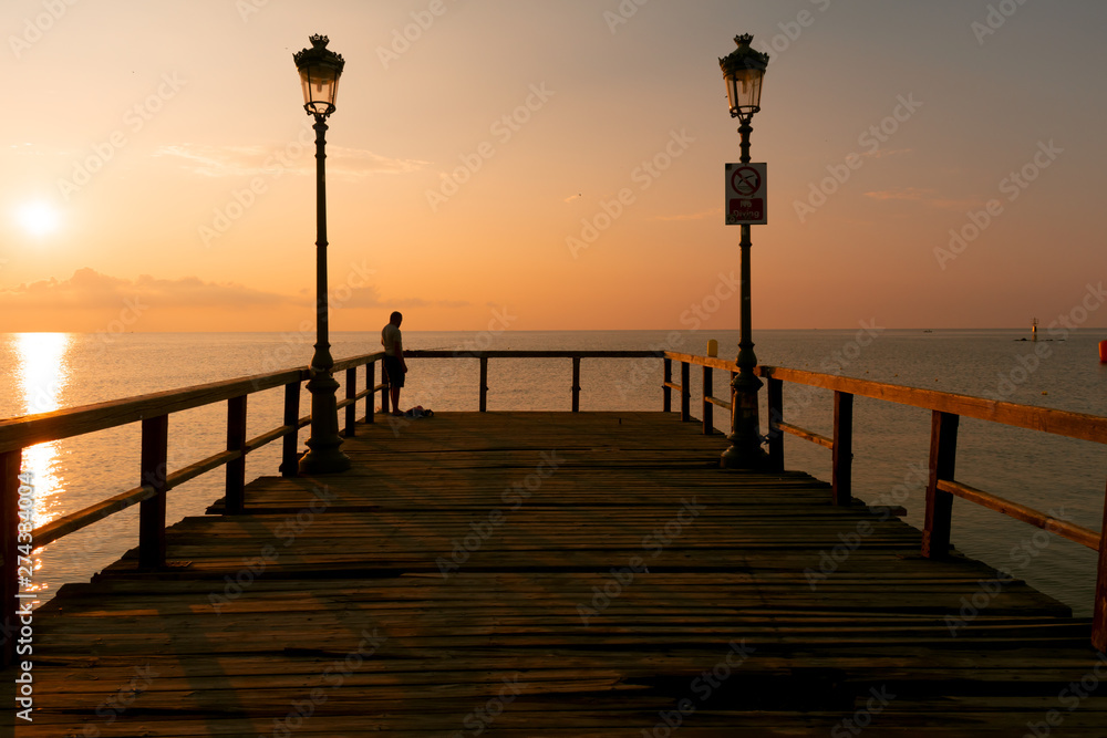 Wooden dock, sea and fisherman in the sunrise. Beautiful summer scenery