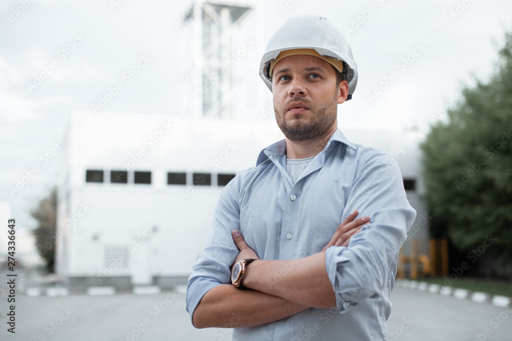 Young handsome male engineer in hardhat standing on the background of water or gas pipes. Concept of boiler station. Pipeline accessories closeup. Heating station manager doing his job outdoor. . Young handsome male engineer in hardhat standing on the background of water or gas pipes. Concept of boiler station. Pipeline accessories closeup. Heating station manager doing his job outdoor. .
